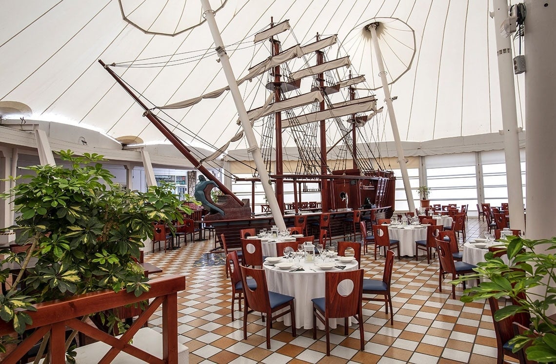 Maritimes Hotelrestaurant mit Schiffsbar, eleganten Tischen und heller Zeltdecke.