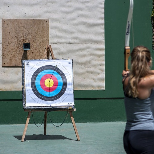 Bogenschießen im Impressive Zocos Lanzarote: Frau zielt auf Zielscheibe, Pfeil im Zentrum.