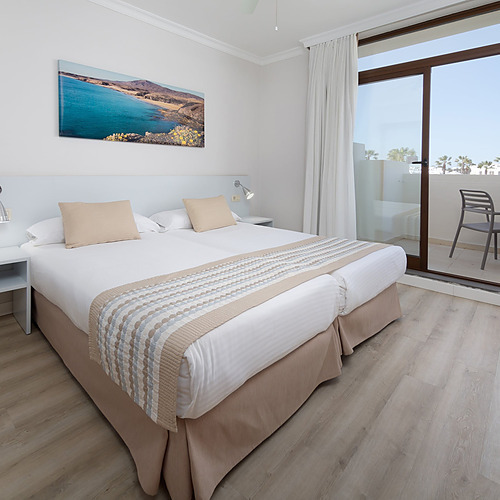 Habitación doble luminosa y moderna en Impressive Zocos Lanzarote, con camas twin, arte mural de paisaje y albornoces.