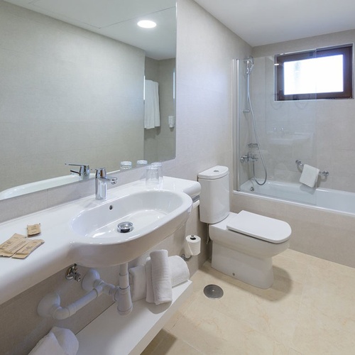 Helles, modernes Badezimmer im Impressive Zocos Lanzarote Hotel mit Badewanne, WC und großem Spiegel.