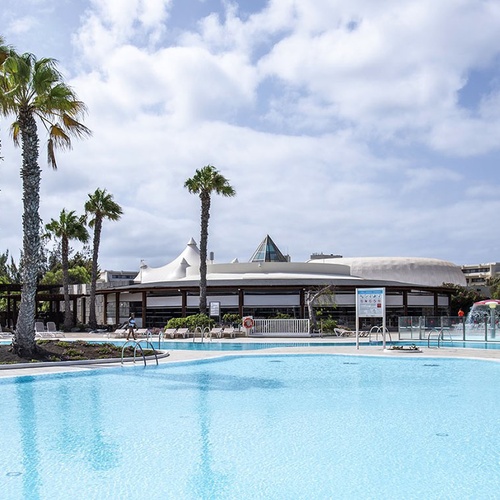 Außenpool des Impressive Zocos Lanzarote mit Palmen und Hotelgebäude unter blauem Himmel.