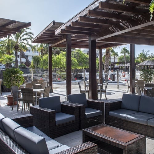 Entspannter Außenbereich des Impressive Zocos Lanzarote mit Pergola und Palmen.