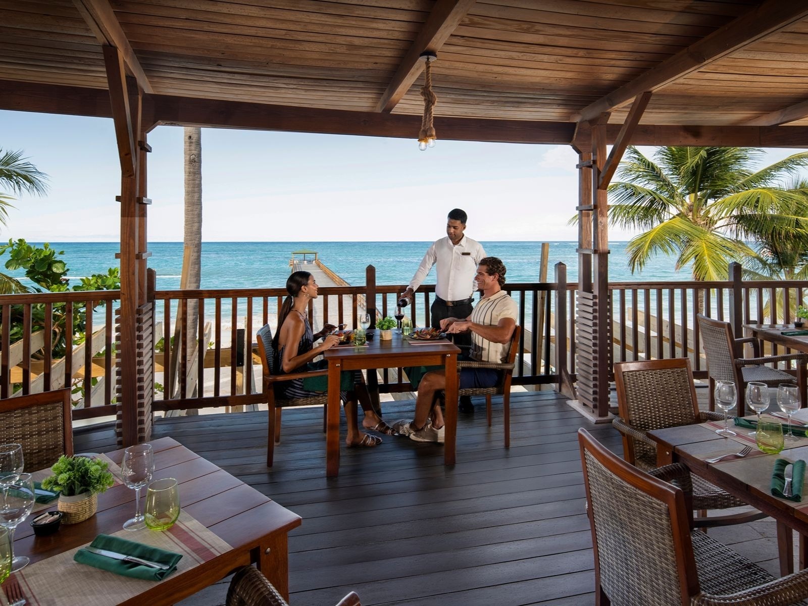 Salle à manger extérieure d'Impressive Resorts & Spas avec vue sur la mer des Caraïbes et les palmiers.