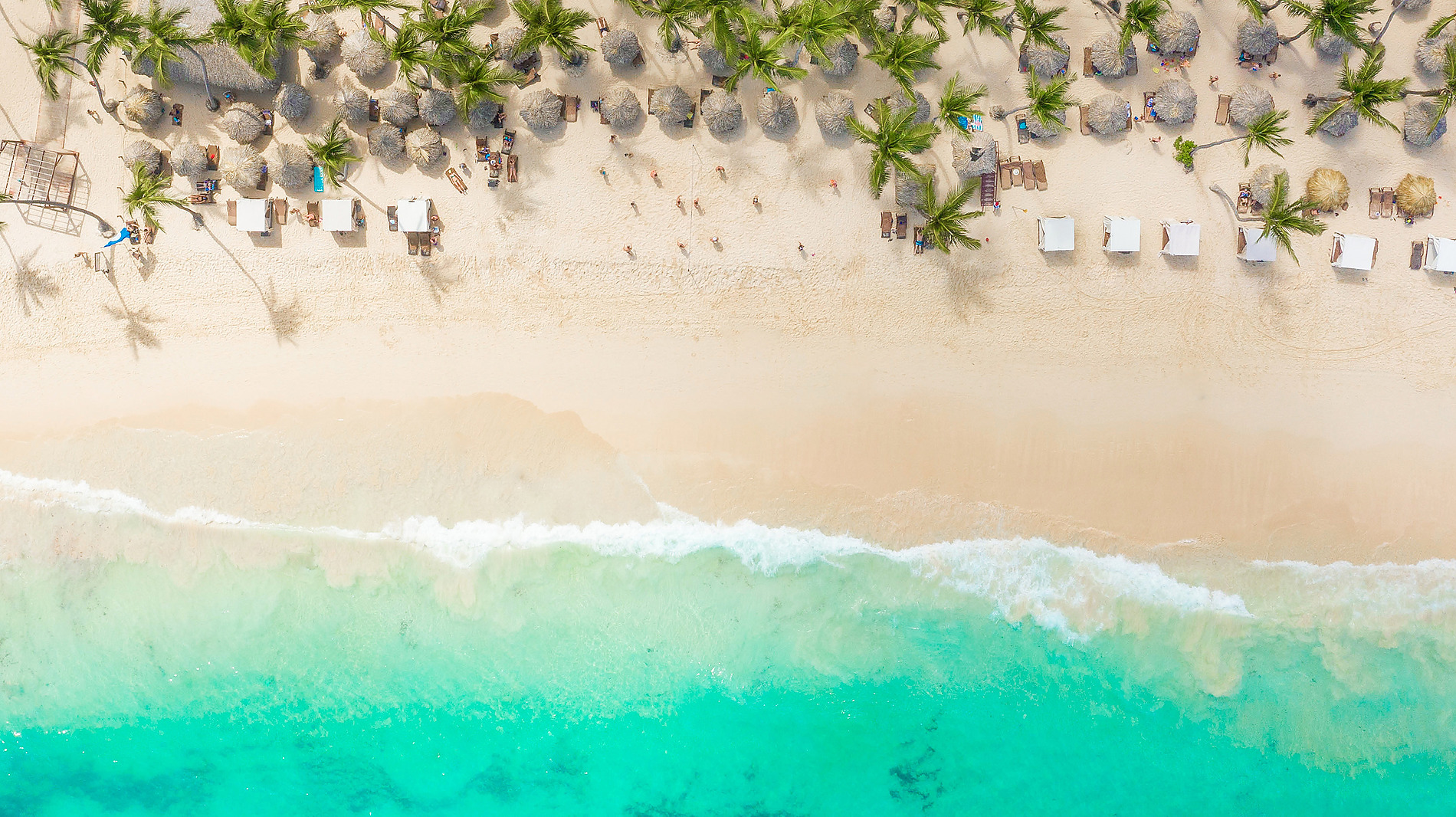 Praia tropical com palmeira e mulher caminhando na água Punta Cana | Impressive Resorts & Spas | Site Oficial