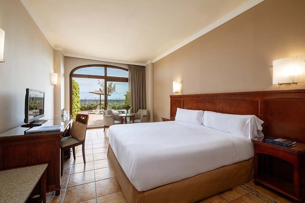 Das Bild zeigt ein helles Hotelzimmer mit einem Doppelbett, einem Schreibtisch und direktem Zugang zu einer Außenterrasse.