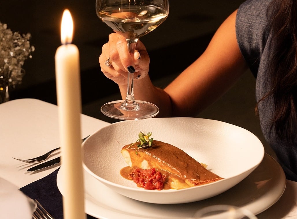 una mujer sostiene un vaso de vino junto a un plato de comida