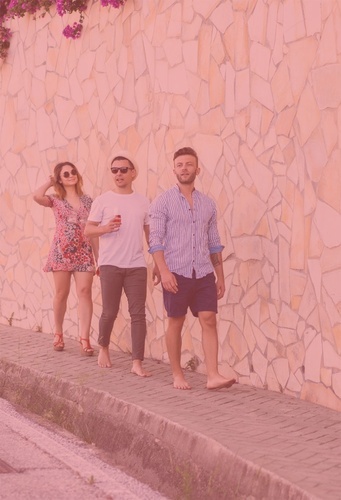 three people walking barefoot on a sidewalk in front of a stone wall