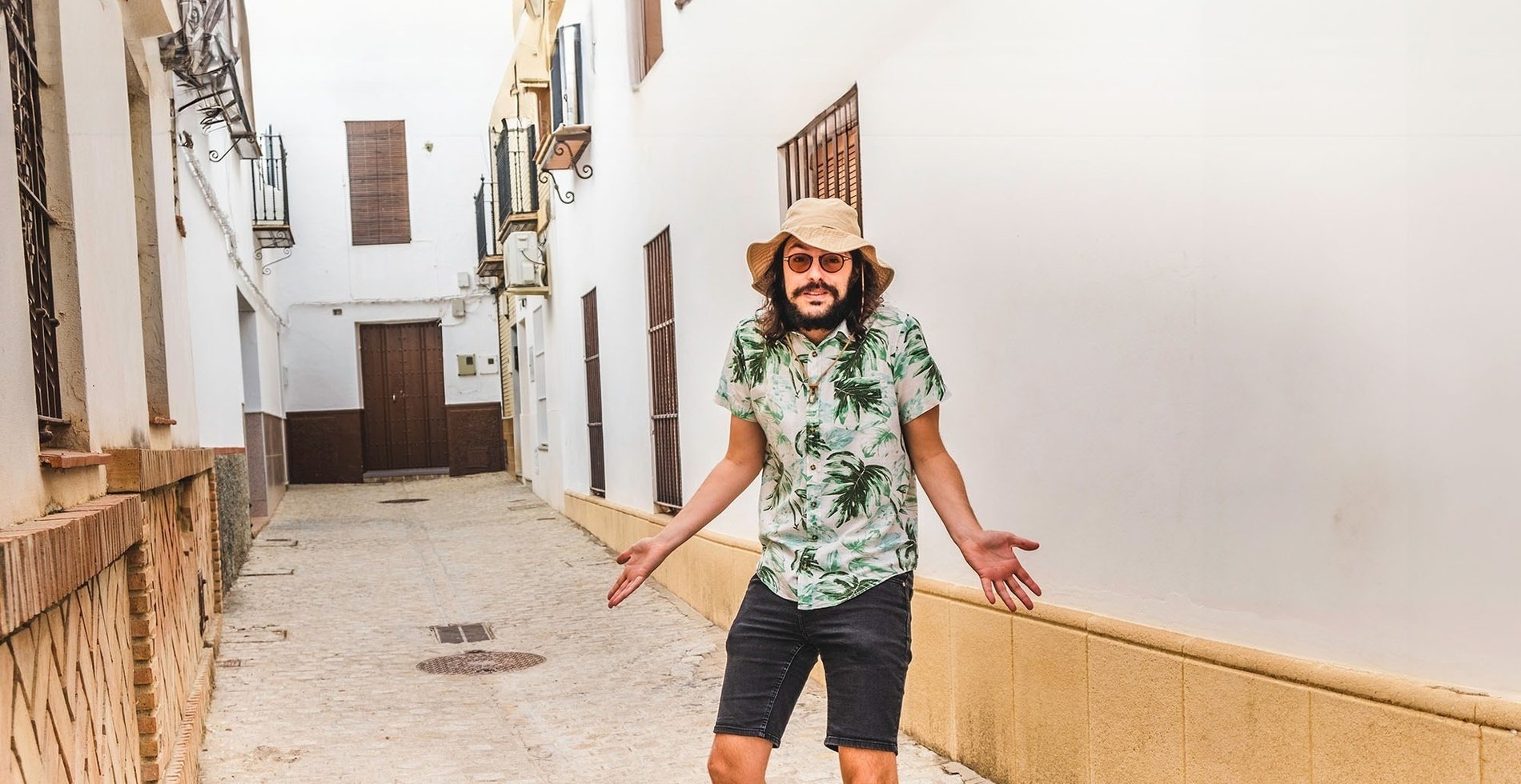un hombre con camisa hawaiana y sombrero camina por un callejón