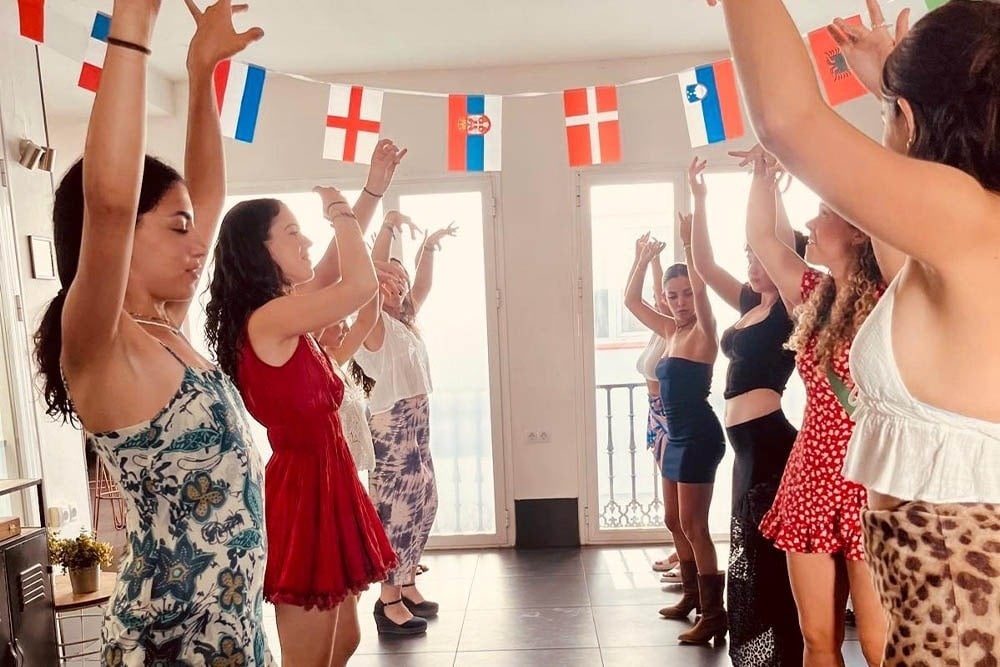 un grupo de mujeres bailan en una habitación con banderas de diferentes países en el fondo