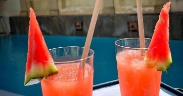 two glasses of watermelon juice with straws in front of a pool