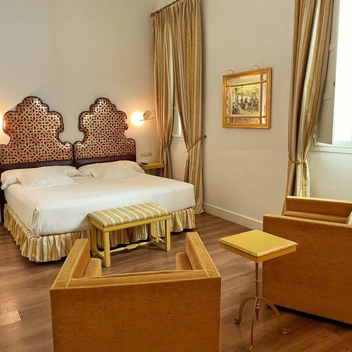 Elegant hotel room in Juderia: Cordoba, featuring a king-size bed, seating, and ornate headboard.