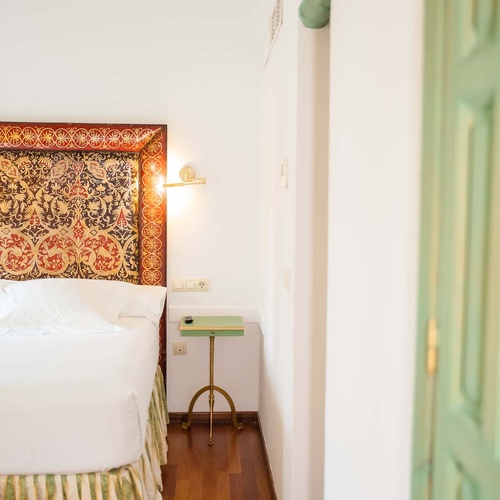 Elegant hotel room with ornate headboard and green accents, near Juderia: Cordoba.