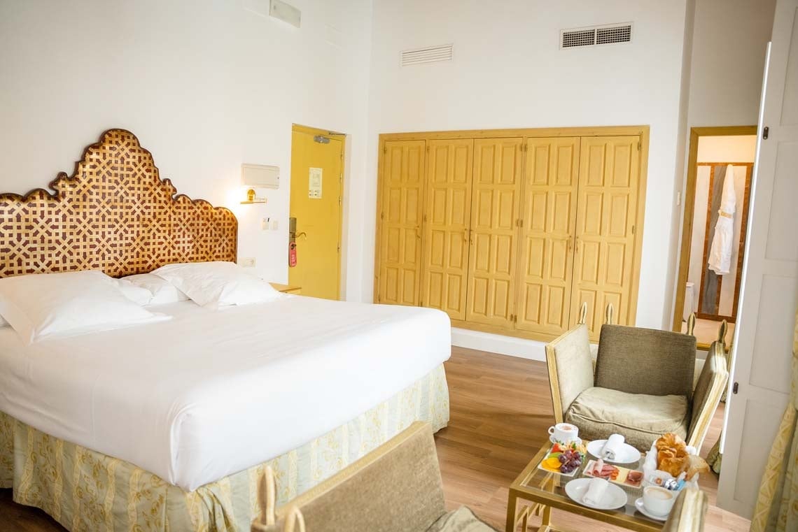 Luxurious hotel room in Juderia: Cordoba with ornate headboard, king bed, and breakfast tray.