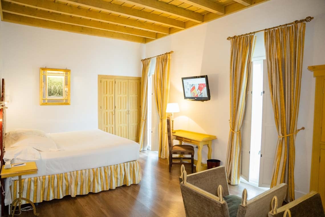 Charming hotel room in Juderia: Cordoba with a king bed, desk, and yellow striped curtains.