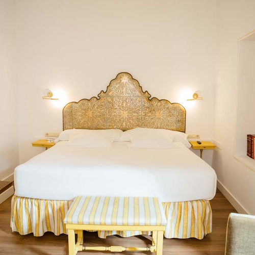 Elegant hotel room in Juderia, Cordoba, with a king-size bed and ornate headboard.