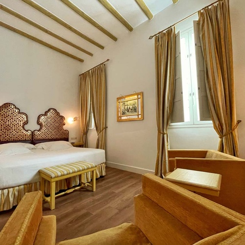 Elegant Juderia: Cordoba hotel room with ornate headboard, plush seating, and city views.