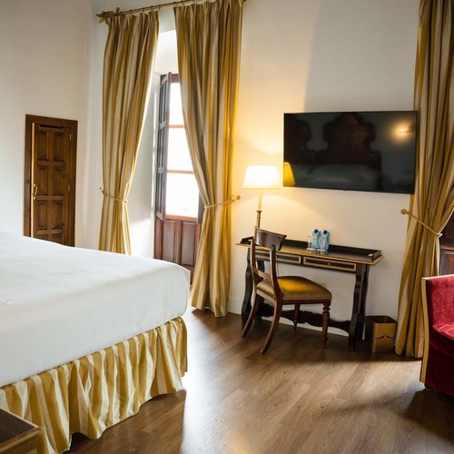 Elegant hotel room with a large bed, desk, and armchair, in the Juderia of Cordoba.