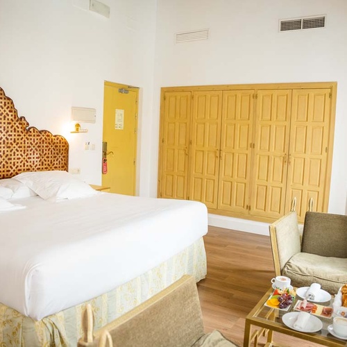 Elegant hotel room in Juderia: Cordoba with a luxurious bed, yellow wardrobe, and breakfast tray.
