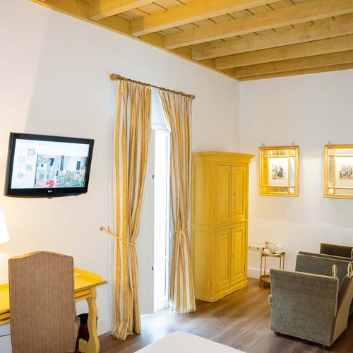 Charming Juderia: Cordoba hotel room with desk, TV, yellow wardrobe & seating.