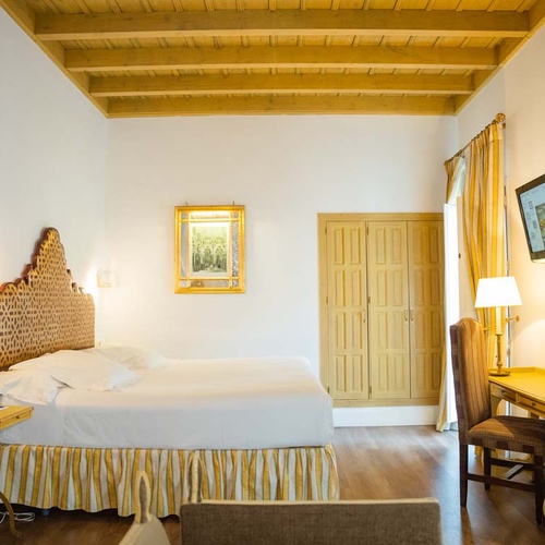 Charming Juderia: Cordoba hotel room with a plush bed, wooden ceiling, and ornate headboard.
