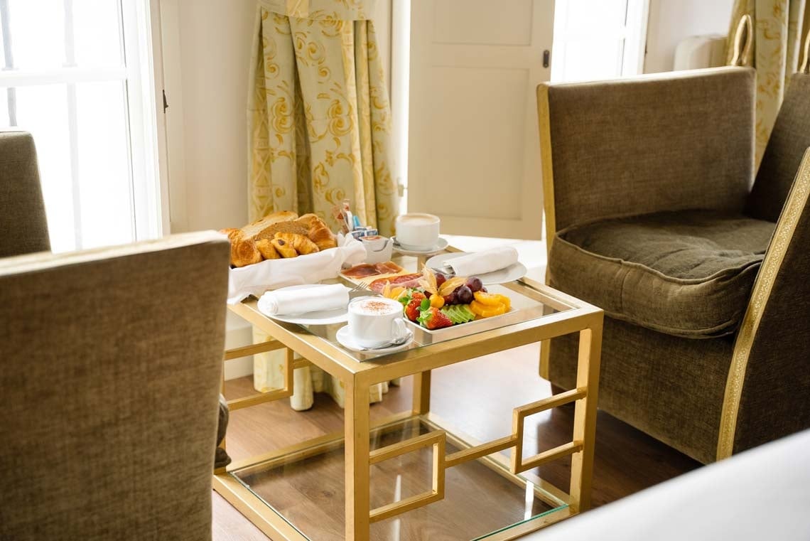 Elegant breakfast tray with fruit, pastries & coffee, set by a window in Juderia: Cordoba hotel.