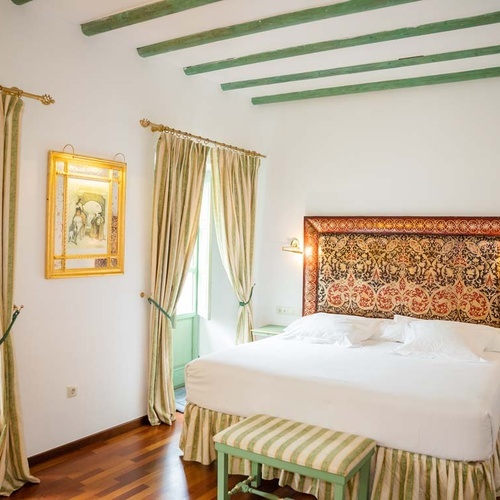 Elegant bedroom in Juderia: Cordoba with ornate headboard, green beams, and antique artwork.