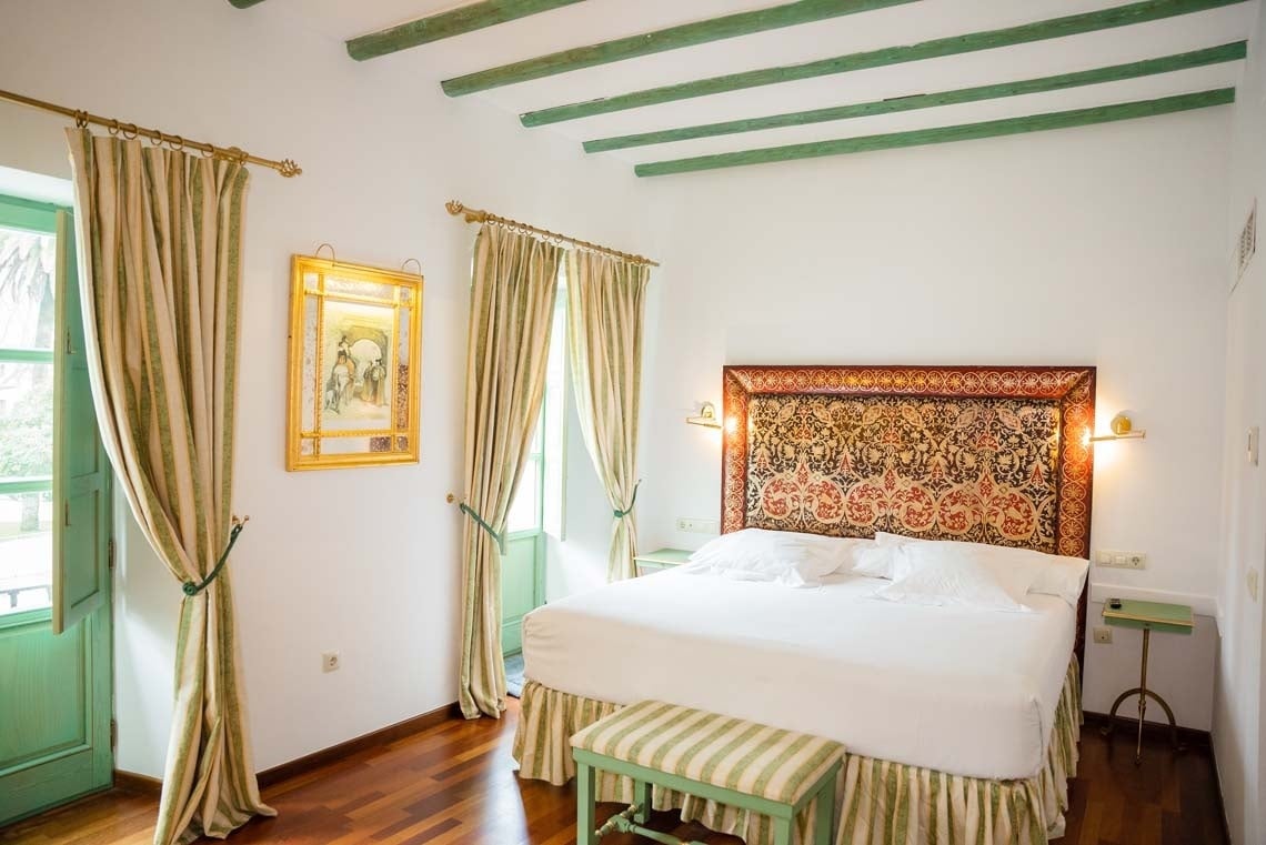Elegant bedroom at Juderia: Cordoba hotel with ornate headboard and striped curtains.