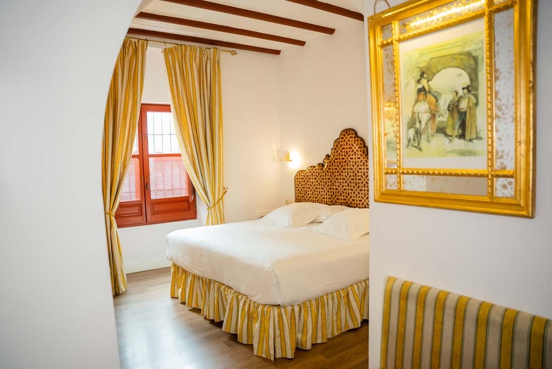 Elegant bedroom in a Juderia: Cordoba hotel, featuring a king bed, yellow striped curtains, and ornate headboard.