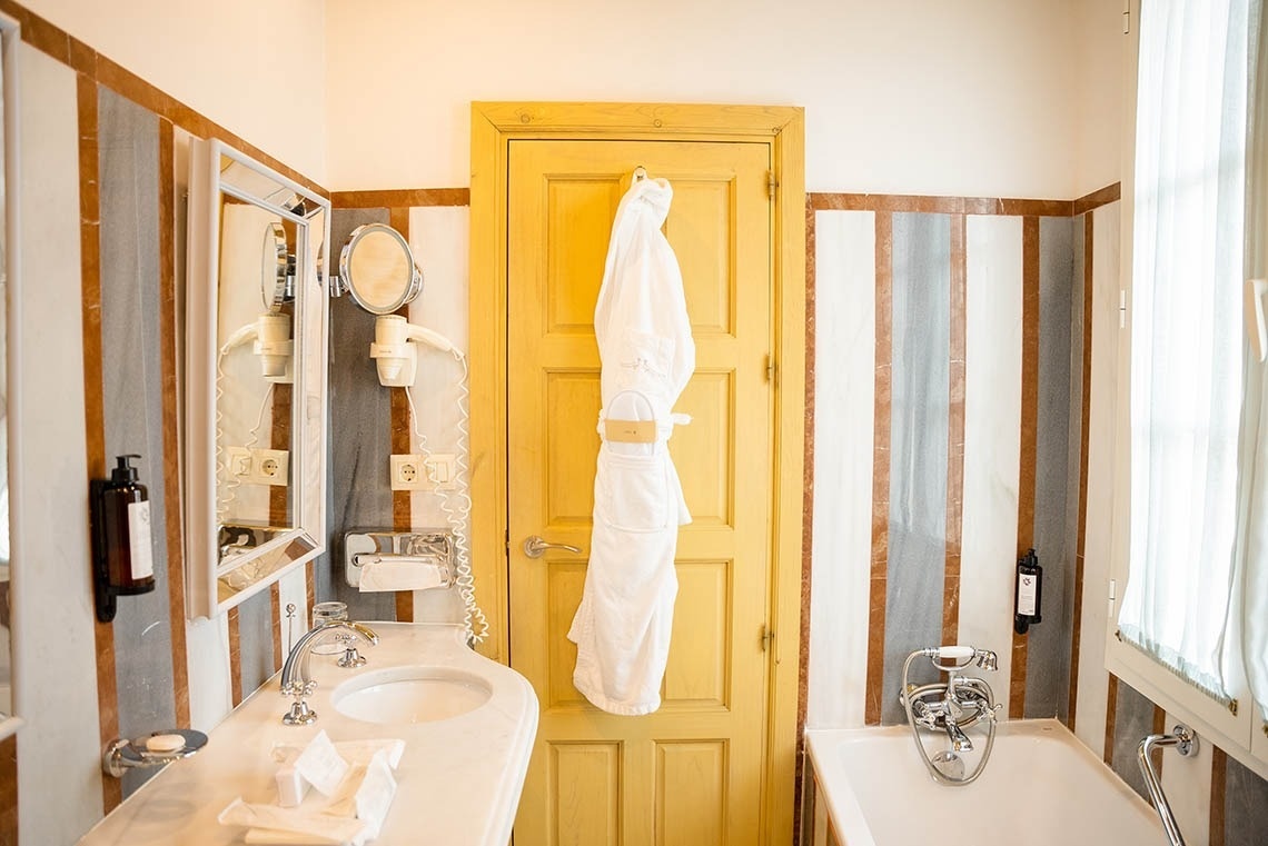 Un cuarto de baño con paredes de rayas de mármol, lavabo, bañera y una puerta amarilla con un albornoz blanco colgado.