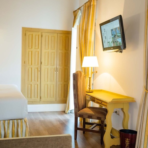 Charming hotel room in Juderia, Cordoba, featuring a desk, TV, and wooden wardrobe.
