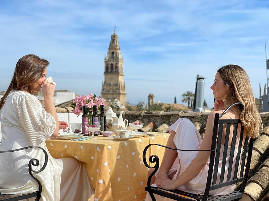 Dos mujeres disfrutan de una bebida en una azotea con vistas a la torre de la Mezquita-Catedral de Córdoba.