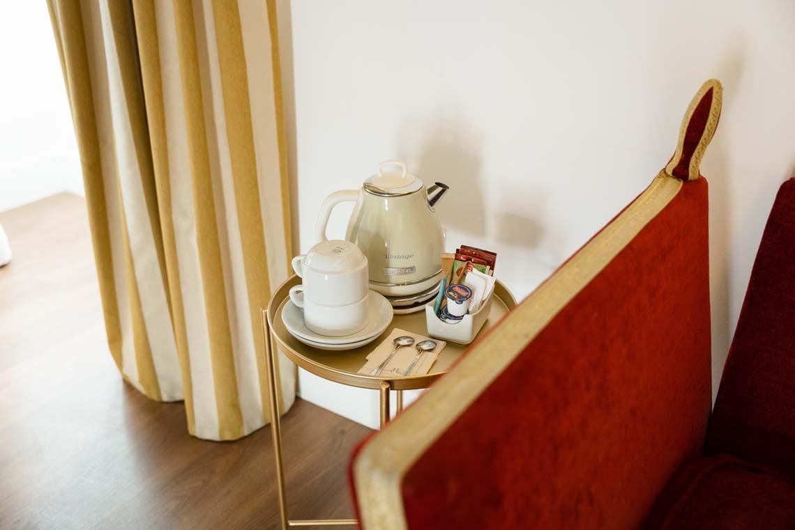 Hotel room amenities in Juderia: Cordoba: Kettle, cups, and coffee/tea on a side table near plush seating.