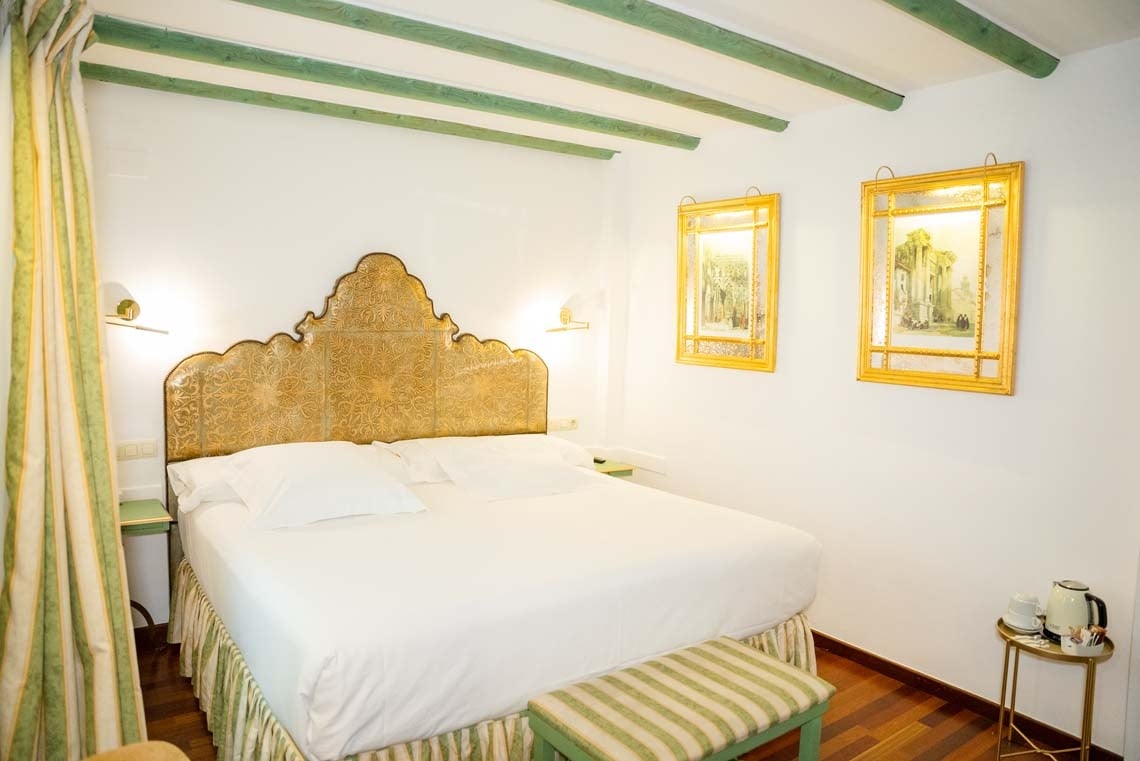 Luxurious Juderia: Cordoba hotel bedroom with ornate headboard & art.