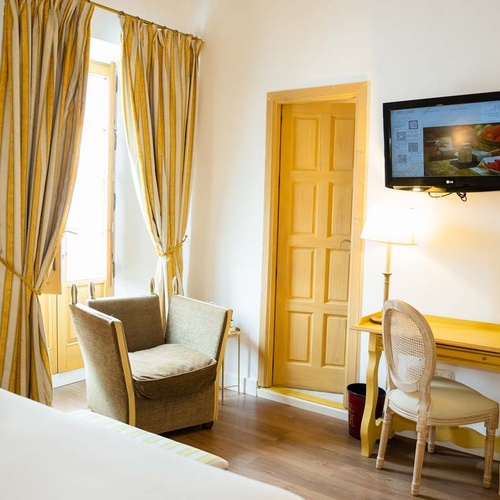 Hotel room in Juderia: Cordoba featuring a desk, chair, armchair, TV, and yellow curtains.