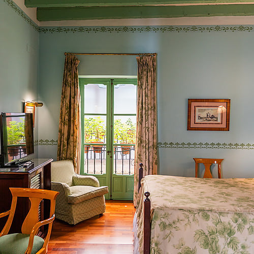 Chambre d'hôtel avec lit fleuri, fauteuil, TV et balcon. Idéal pour un séjour reposant. Juderia: Sevilla
