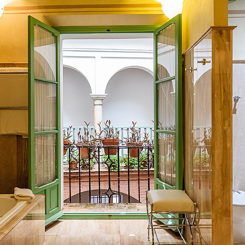 Salle de bain luxueuse avec vue sur cour intérieure et balcon fleuri. Plongez dans le confort de notre hôtel Juderia: Sevilla.