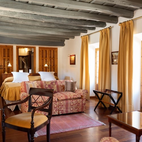 Elegant room at Juderia: Sevilla hotel, featuring antique wood beams, patterned curtains, and a cozy seating area.