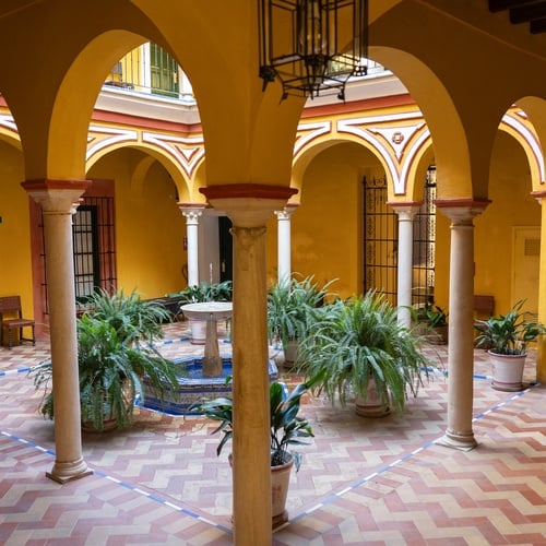 Courtyard of a Sevilla Juderia hotel, featuring arches, a fountain, and potted ferns.