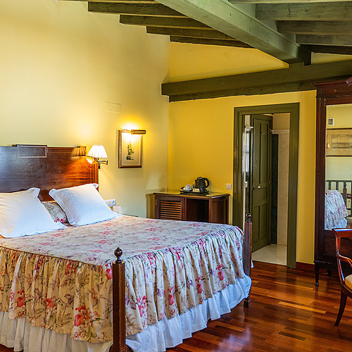 Chambre d'hôtel confortable avec lit double fleuri, bois sombre et télévision. Idéal pour votre Juderia: Sevilla.