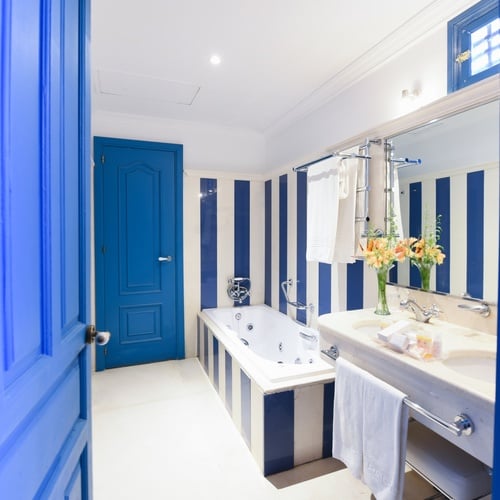 Bright blue door opens to a modern bathroom with bathtub, sink, and striped walls. Juderia: Sevilla.