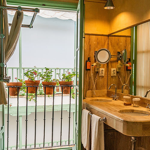 Salle de bain luxueuse avec double vasque en marbre et balcon fleuri. Un espace parfait pour un séjour tout confort. Juderia: Sevilla