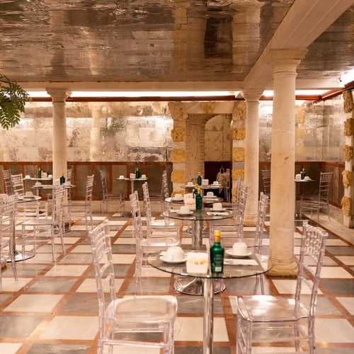 Elegant dining area in the Judería: Sevilla, with glass tables, crystal chairs, and ancient stone columns.