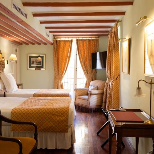 Elegant Juderia: Sevilla hotel room with two beds, vintage armchair, and classic decor.