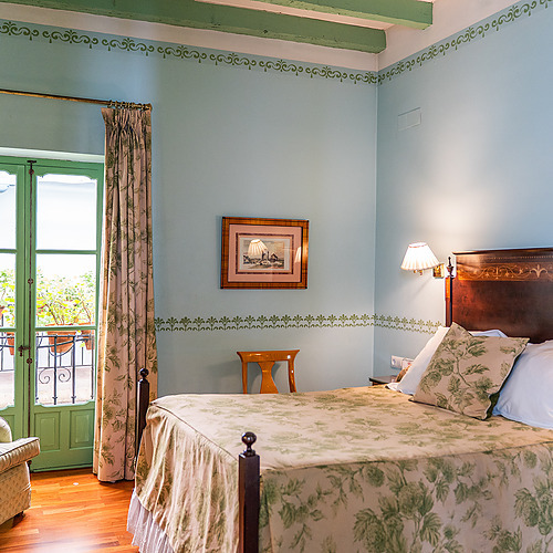 Chambre d'hôtel confortable avec lit, fauteuil et balcon fleuri, parfaite pour votre Juderia: Sevilla.