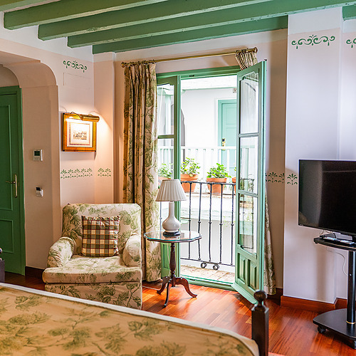 Chambre d'hôtel avec balcon, fauteuil fleuri, lit, télévision et décorations murales. Votre Juderia: Sevilla parfait.