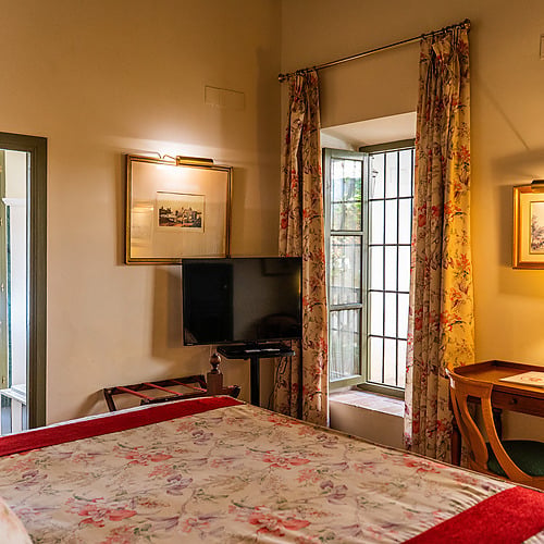 Chambre d'hôtel confortable avec lit fleuri, TV, bureau et fenêtre, idéale pour un séjour Juderia: Sevilla.