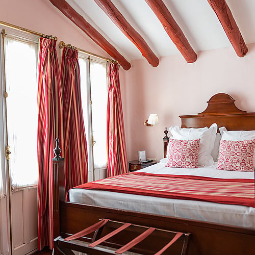 Lit d'hôtel classique avec des poutres apparentes rouges, des rideaux rayés et un couvre-lit rouge. Juderia: Sevilla