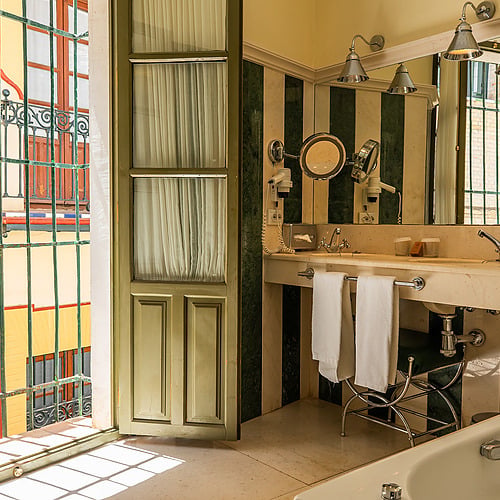 Salle de bain luxueuse avec vue sur un balcon orné, miroir, baignoire et lavabo. Juderia: Sevilla