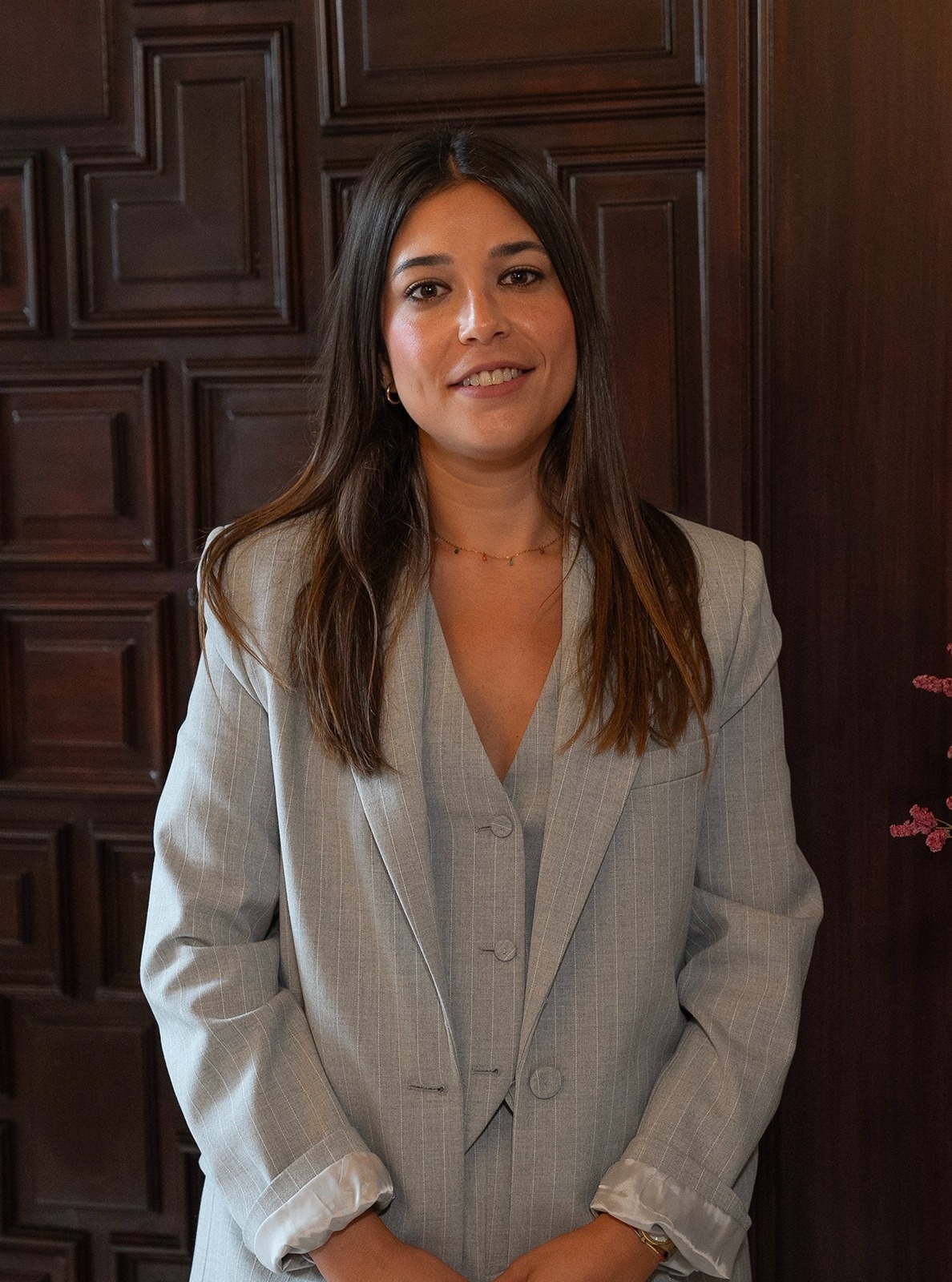  a woman in a suit is smiling in front of a wooden wall 