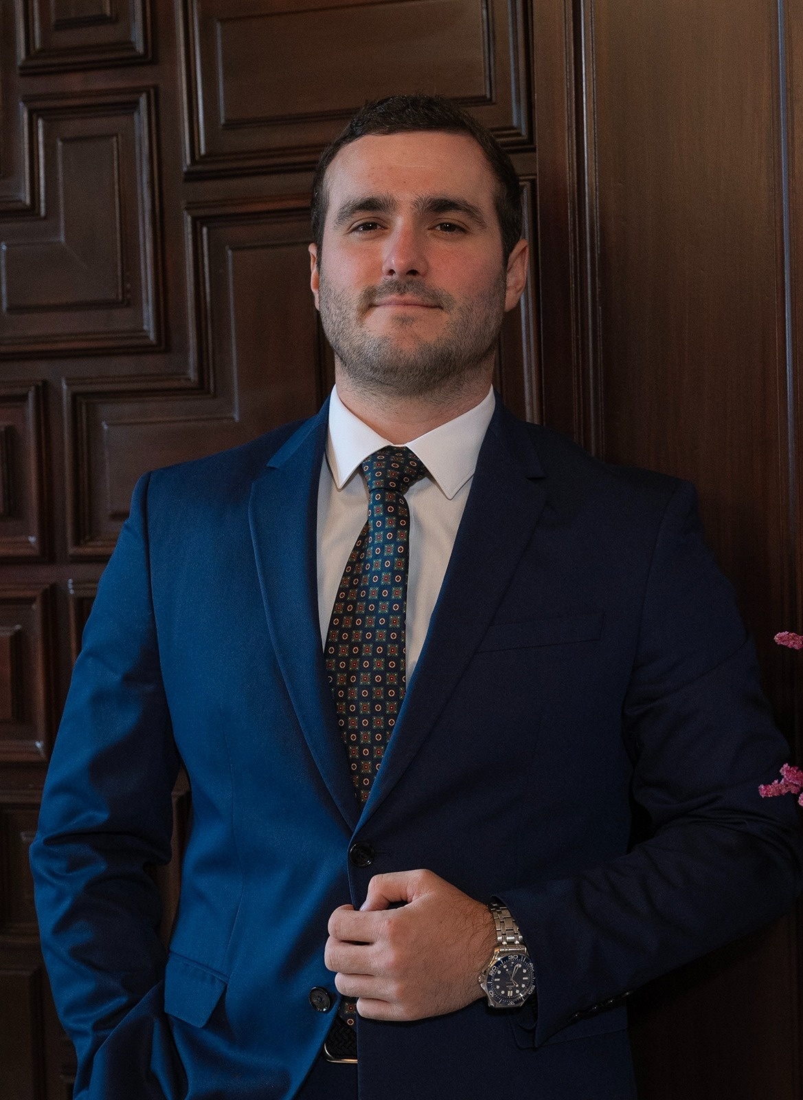  a man in a suit and tie is standing in front of a wooden door 
